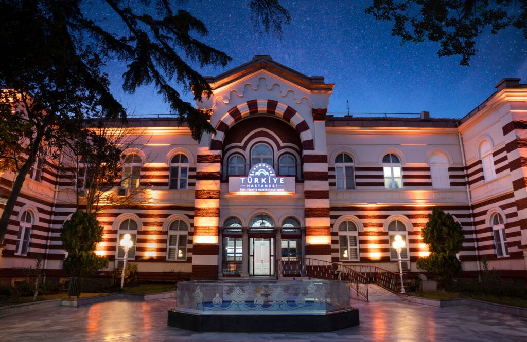 Türkiye Hastanesi'nin gece görseli, aydınlatmalı cephe ve yıldızlı gökyüzü manzarası.