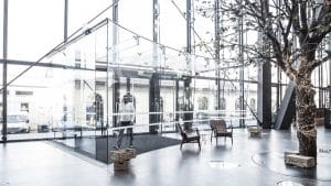 Haberler & Blog 19 Modern ofis lobisi giriş kapısı, cam duvarlar, ağaç detayı ve rahat oturma alanlarıyla aydınlık bir alan sunuyor.