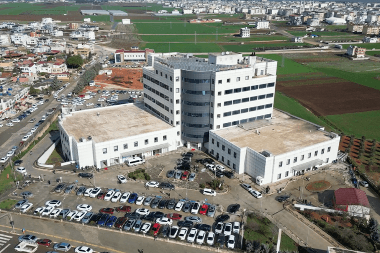 Hastane binası ve çevresindeki otopark, geniş bir alandan drone ile çekilmiş hava fotoğrafı.