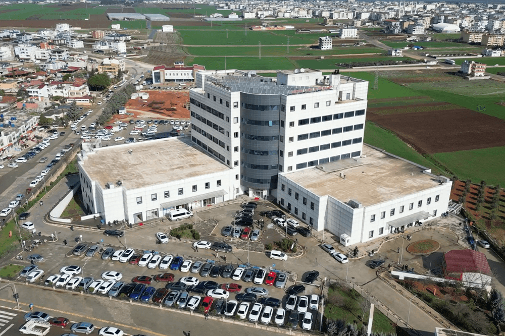 Hastane binası ve çevresindeki otopark, geniş bir alandan drone ile çekilmiş hava fotoğrafı.