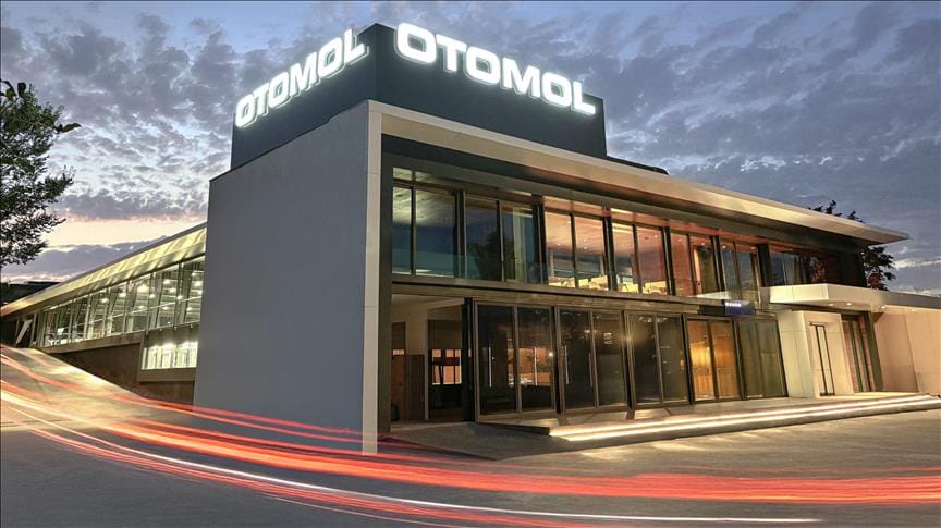 Modern bir otomobil galerisinin akşam vakti dış cephesi, Otomol tabelasıyla aydınlanıyor.